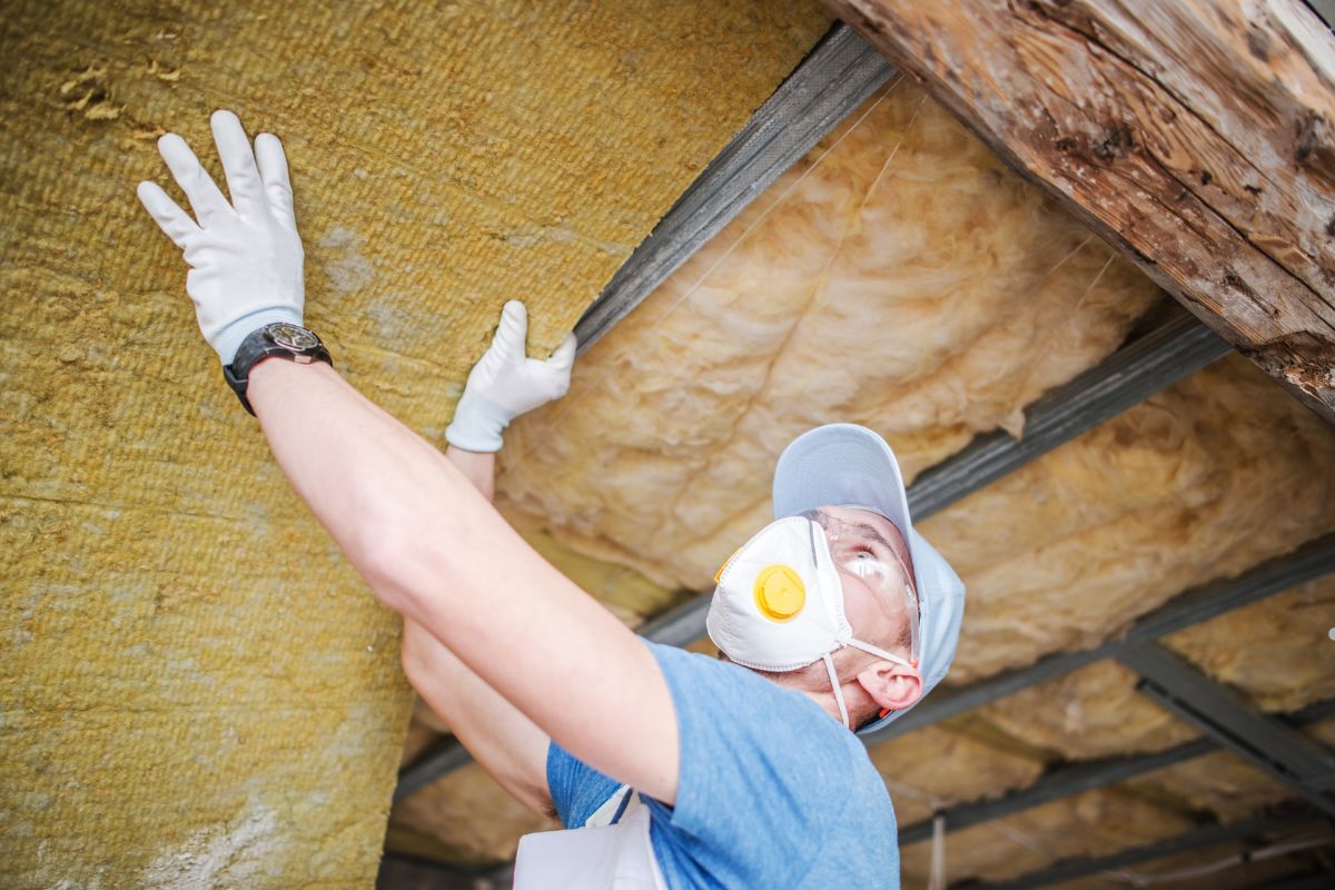 A man in a mask and gloves installs insulation, demonstrating safety in an insulation service setting.
